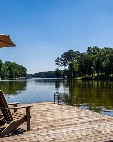 Wooden dock with Adirondack chairs and umbrella overlooking calm river lined with trees