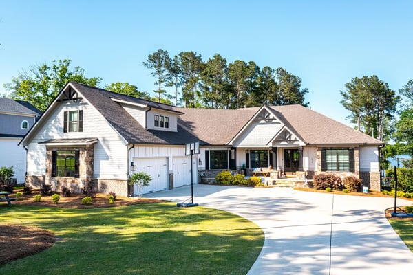 Modern farmhouse with white siding, dark roof, brick accents, two-car garage, and front porch overlooking manicured lawn and pine trees.
